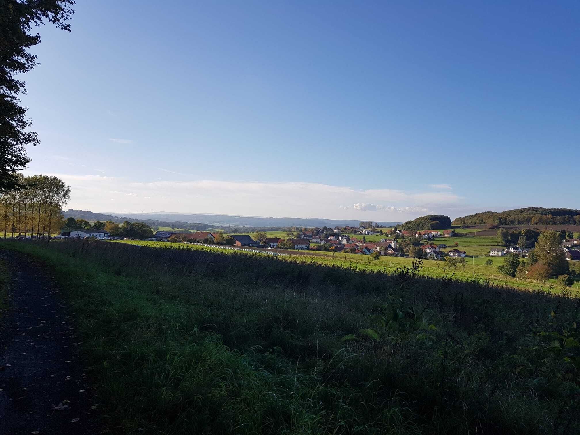 Landskab med huse, marker og en klar himmel.