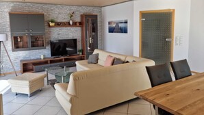 A modern living room with a sofa, TV, and wooden dining table. - Ferienwohnung "schöne Aussicht" in der Rhön (Kalbach)