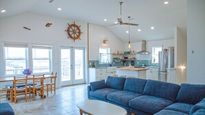 Een ruime woonkamer met een grote blauwe bank, een houten eettafel met stoelen, en een keuken op de achtergrond.