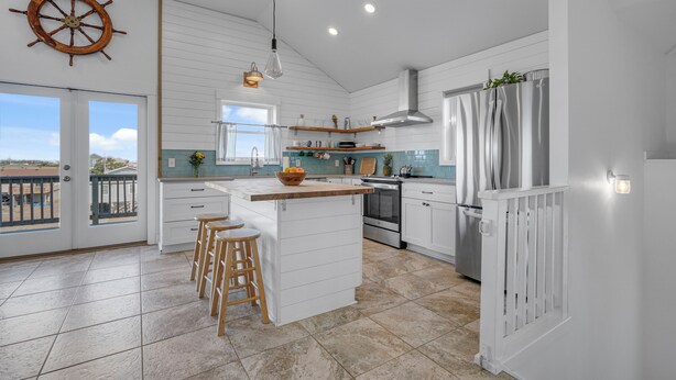 Een moderne keuken met een centraal eiland, witte keukenkastjes, een decoratie van een roerpropeller en uitzicht naar buiten.