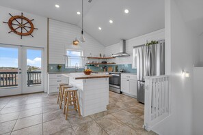 Une cuisine moderne dotée d’un îlot central, de meubles blancs et d’une décoration en forme de barre de timon, avec vue sur l’extérieur.