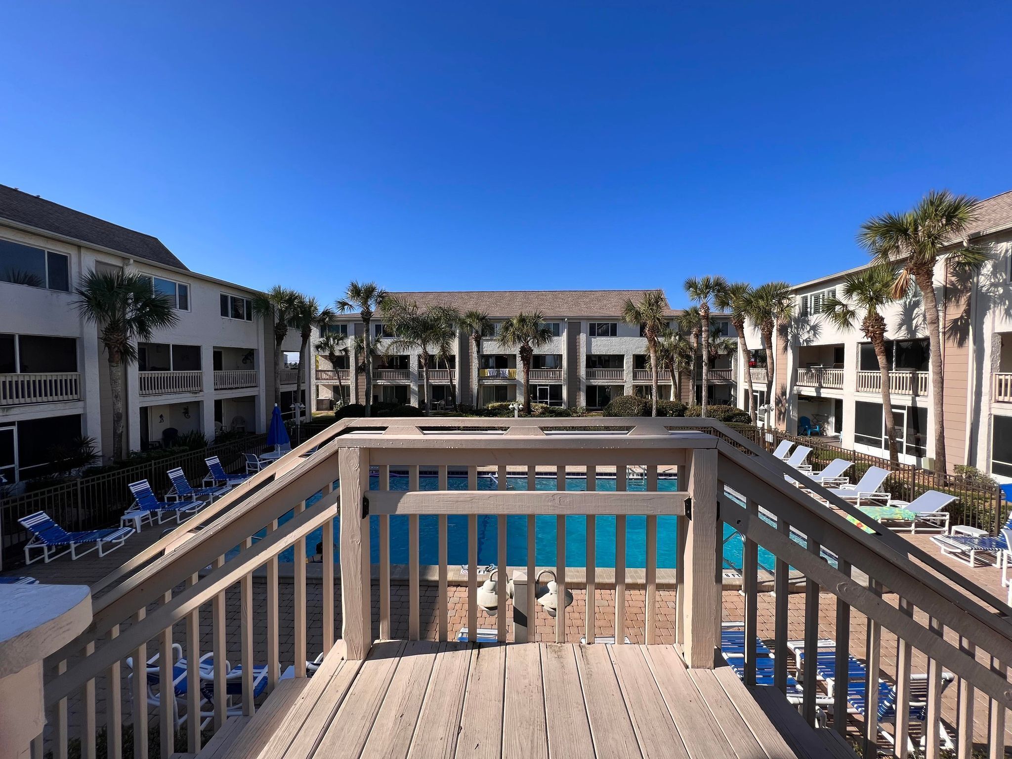 A poolside area with wooden deck, lounge chairs, and a clear blue pool.