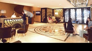 En hotellobby med reception, siddeområde og dekorativt loft.