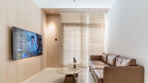 En moderne stue med et fladskærms-tv monteret på væggen, en lædersofa, et rundt sofabord og en skydedør med persienner.