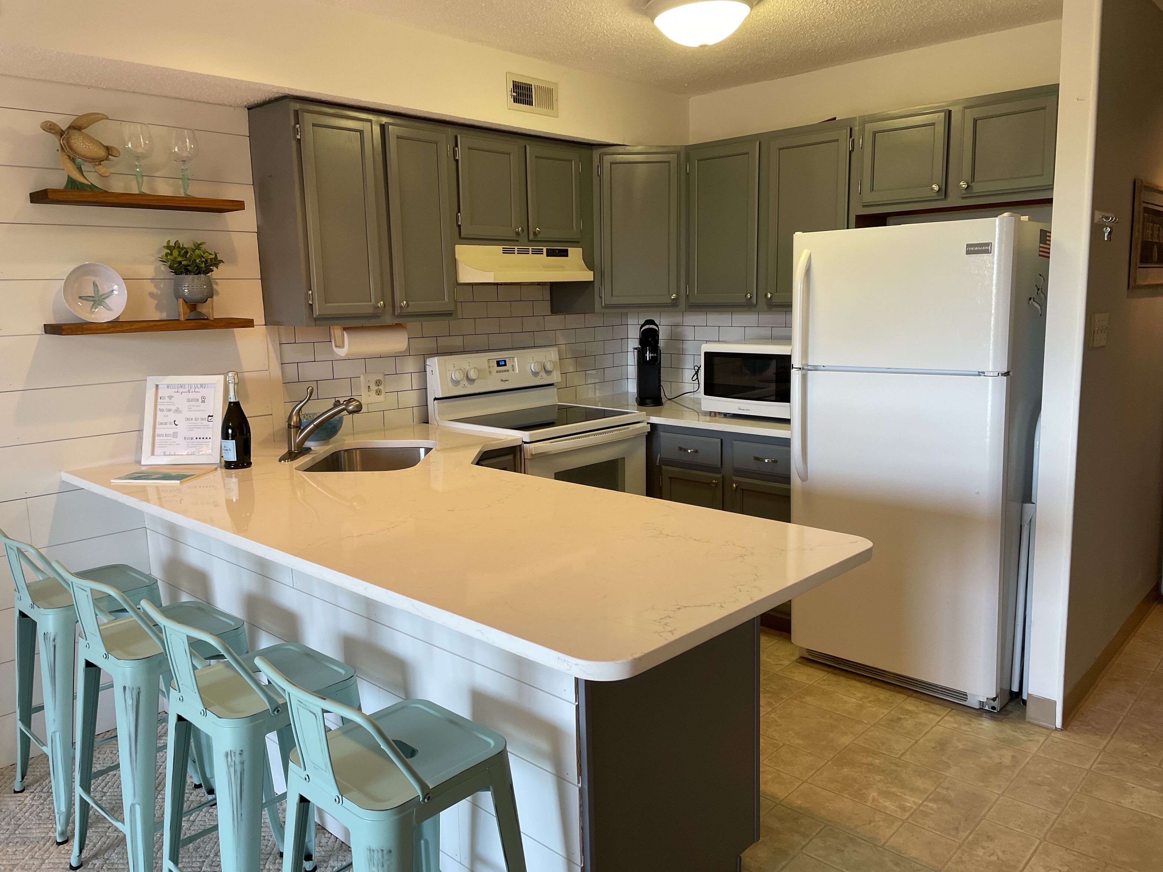 Una cocina con isla central, taburetes de bar, refrigerador y microondas.