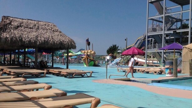 Ein Poolbereich mit Liegestühlen, einer Struktur mit Reetdach und einer Wasserrutsche.
