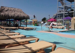 Ein Poolbereich mit Liegestühlen, einer Struktur mit Reetdach und einer Wasserrutsche.