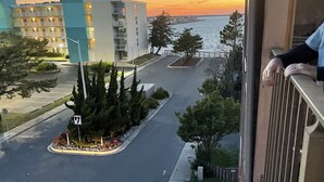 Blick auf eine Stadtstraße bei Sonnenuntergang, mit Gebäuden, einem Parkplatz und einem Gewässer in der Ferne.