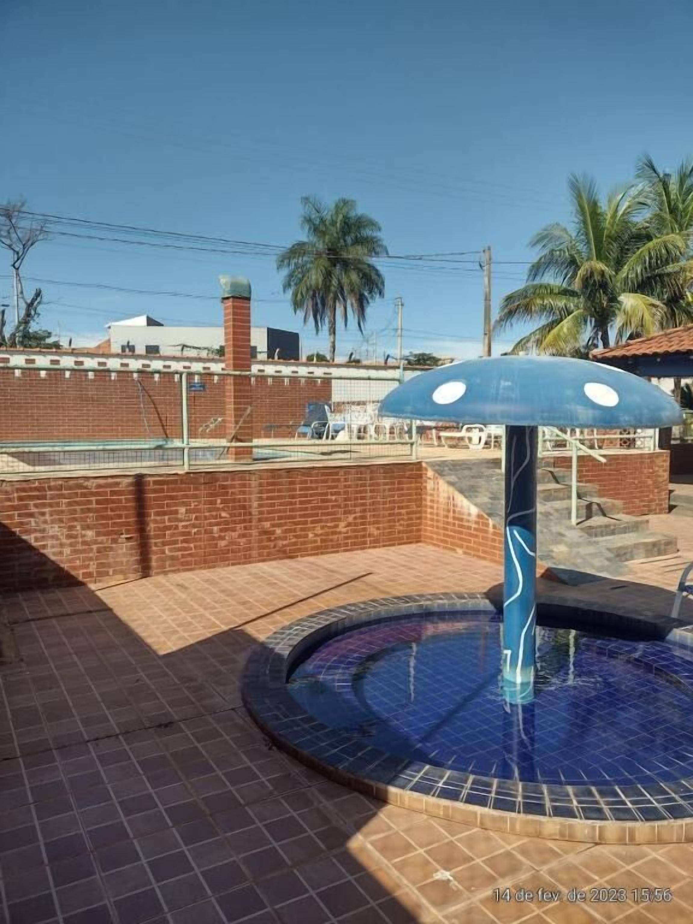 A swimming pool with a blue umbrella, surrounded by a brick wall and palm trees.