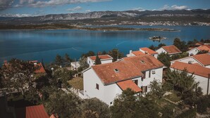 A coastal village with white buildings and red roofs, a large body of water, and mountains in the background.