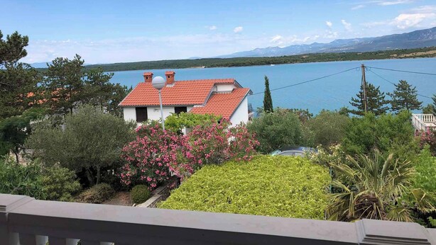 A house with a red roof, surrounded by lush greenery and a view of a lake and mountains.