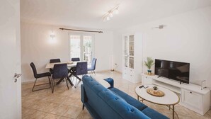 A modern living room with a sofa, TV, dining table, chairs, and a cabinet.