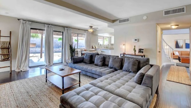 A spacious living room with a large grey sectional sofa, a coffee table, and a dining area with a white table and chairs. - Spacious Home with Heated Pool! (Henderson)