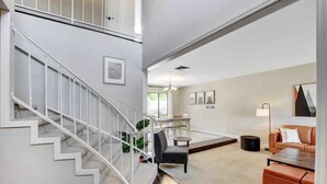 A modern interior with a staircase, a dining area, and a seating area with a sofa and coffee table. - Spacious Home with Heated Pool! (Henderson)