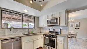 A modern kitchen with white cabinets, stainless steel appliances, and a large window. - Spacious Home with Heated Pool! (Henderson)