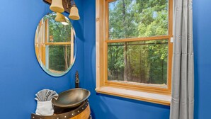 Une salle de bain avec une grande fenêtre, un miroir rond et un tonneau en bois servant de porte-serviettes.