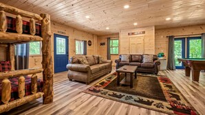 L’intérieur d’une cabane en rondins comprend deux canapés, une table basse, une table de billard et une terrasse en bois.