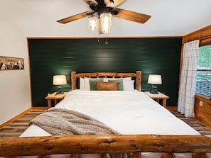 Una cama con estructura de madera, cabecera verde, dos lámparas de noche y un ventilador de techo con tres luces.
