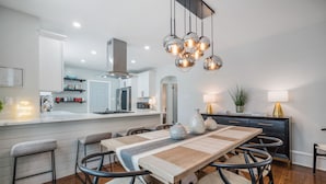 Una cocina moderna con una isla central, iluminación colgante y un comedor con mesa y sillas de madera.