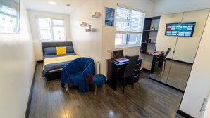 A modern bedroom with a bed, a desk, and a computer. There is a window with blinds, a mirror, and a TV mounted on the wall. - Cosy Studio Close to University of Birmingham (Birmingham)