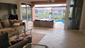 Amplia sala de estar con una gran mesa de centro de vidrio, un sofá y vistas a una piscina y una casa a través de grandes puertas correderas de cristal.