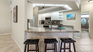 Una cocina moderna con una isla central, taburetes de bar y vistas al área de estar.