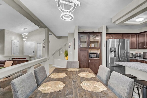 A modern kitchen with stainless steel appliances, a dining area with a wooden table and gray chairs, and a staircase leading to an upper level.