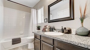 A bathroom with a bathtub, toilet, vanity with a sink, and a large mirror.