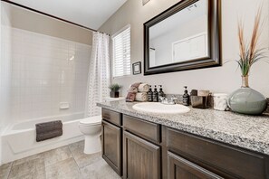 A bathroom with a bathtub, toilet, vanity with a sink, and a large mirror.