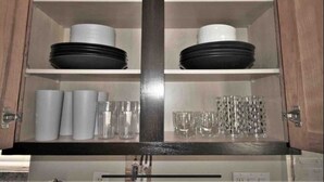 A kitchen cabinet with two shelves, each holding plates, bowls, and glasses.
