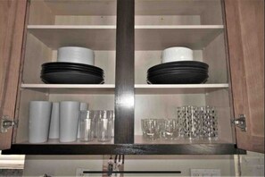 A kitchen cabinet with two shelves, each holding plates, bowls, and glasses.