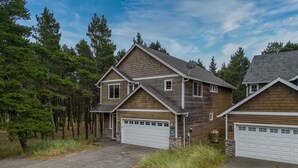 A two-story house with a garage, surrounded by trees and a driveway. - Spacious 2-Story Home, walk to the beach, fenced yard, patio, bbq and fire pit (Pacific City)