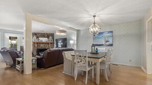 A spacious living area with a fireplace, a dining table with chairs, and a large painting on the wall. - Lakefront Townhome with Stunning Sunsets – StillWaters on Lake Martin (Dadeville)