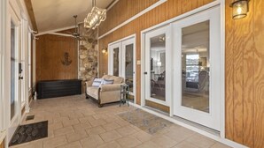 A covered outdoor area with a stone wall, a sofa, and a sliding glass door leading to a room. - Lakefront Townhome with Stunning Sunsets – StillWaters on Lake Martin (Dadeville)