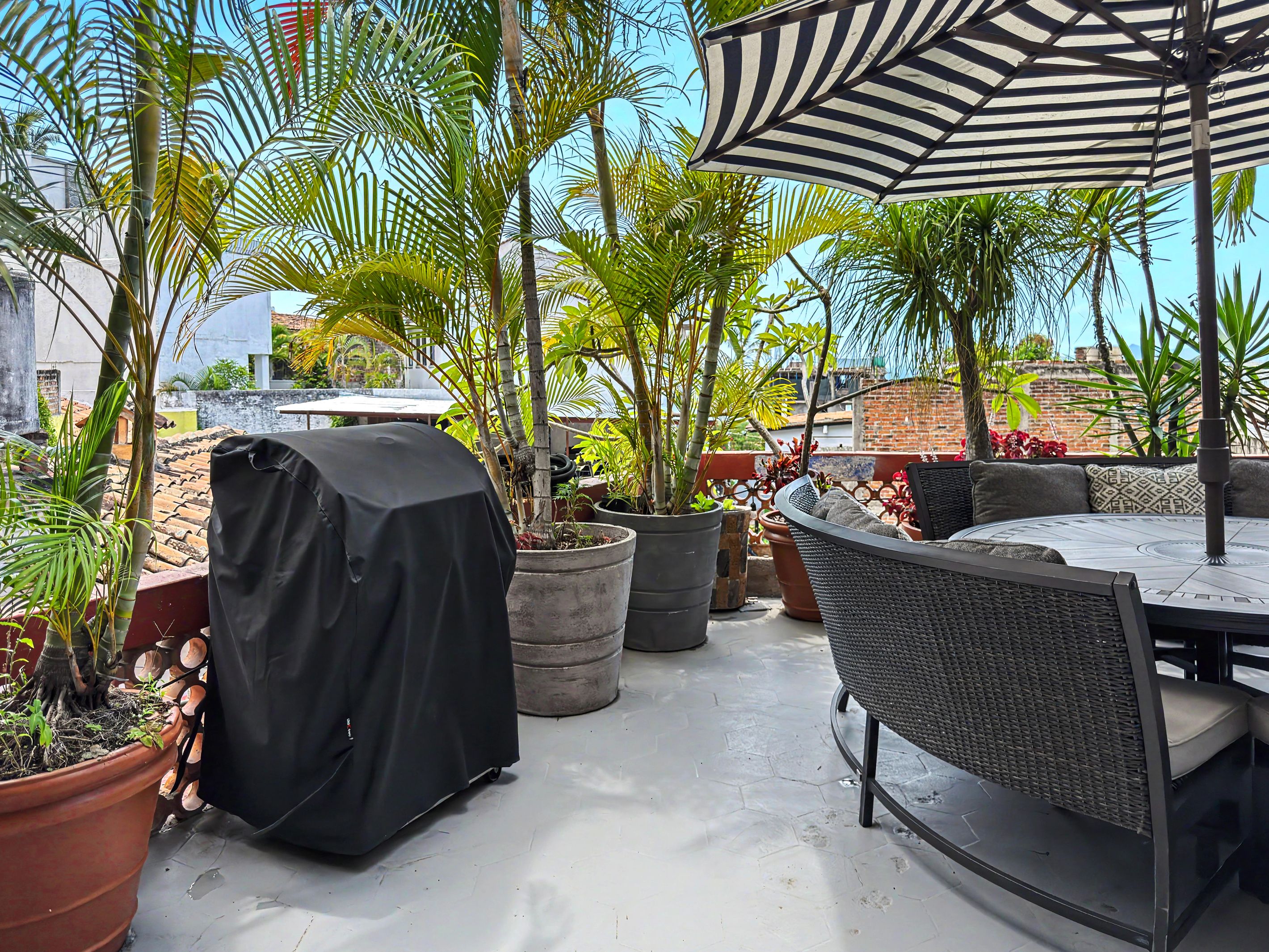 A patio with outdoor furniture, potted plants, and a striped umbrella.