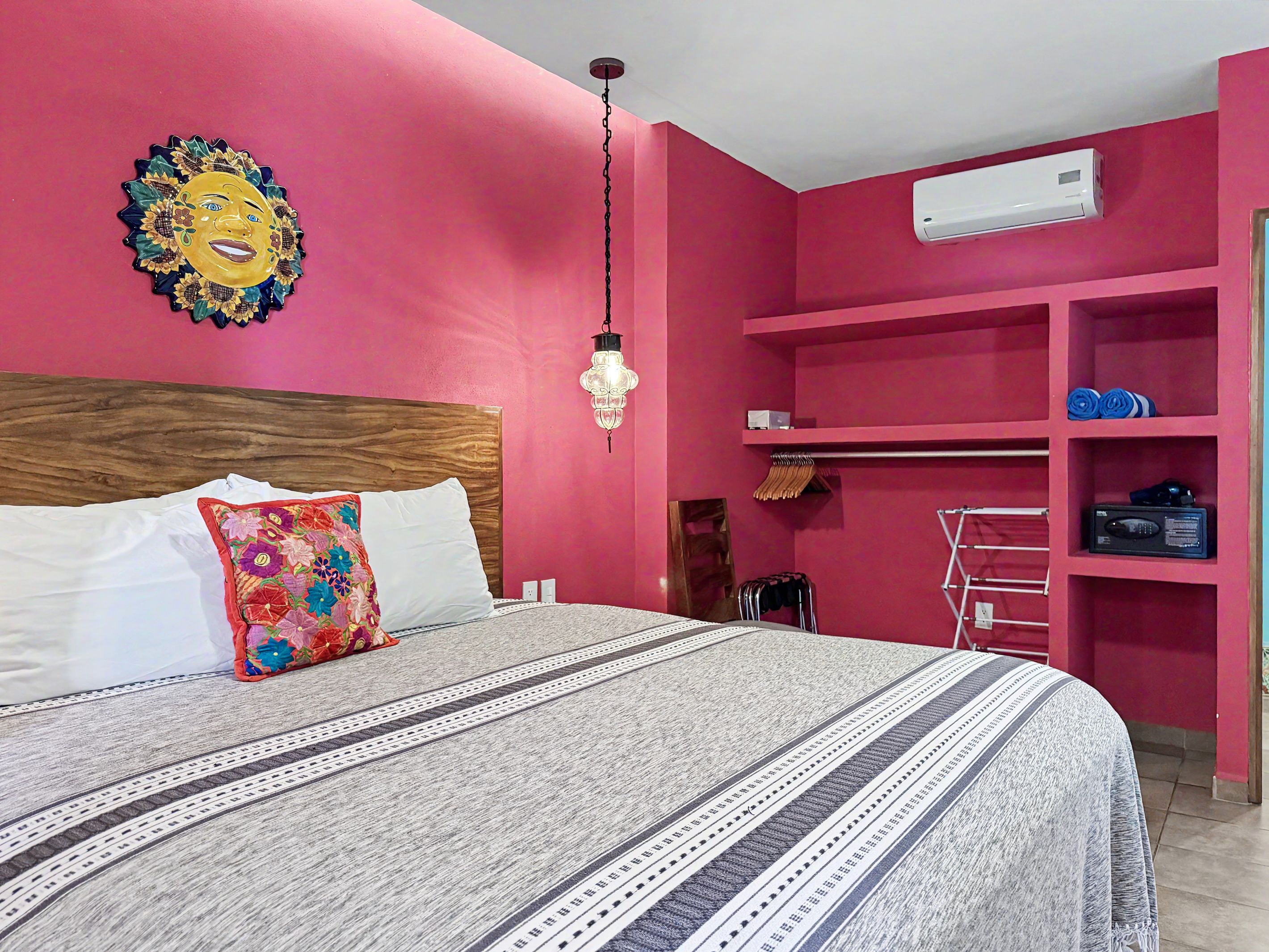 Une chambre à coucher avec un lit, un climatiseur fixé au mur et une étagère où sont pliés des vêtements.