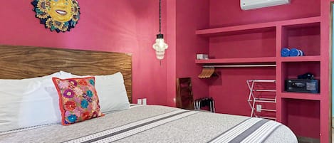 A bedroom with a bed, a wall-mounted air conditioner, and a shelf with folded clothes.