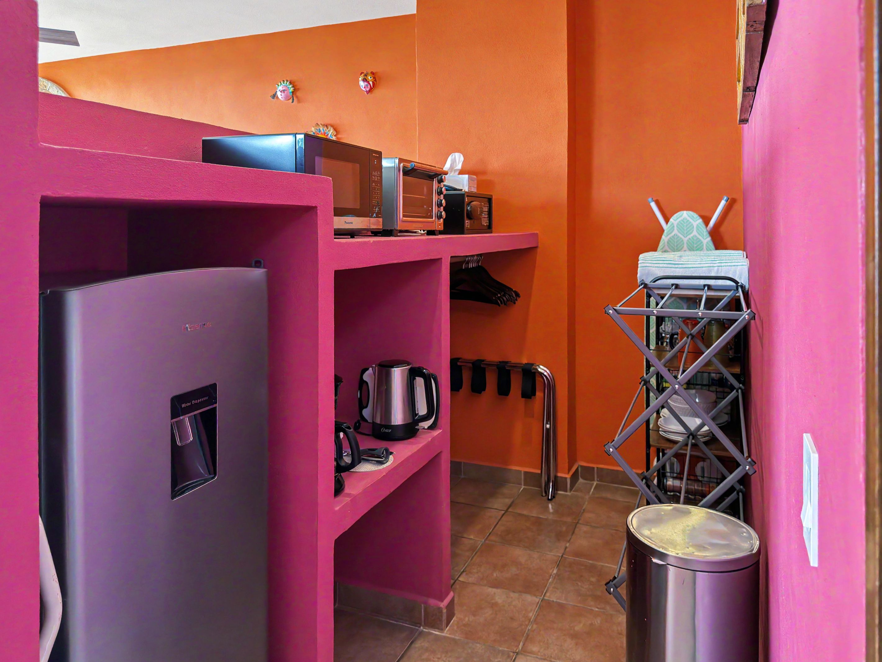 A compact kitchen with a refrigerator, microwave, kettle, and a drying rack.