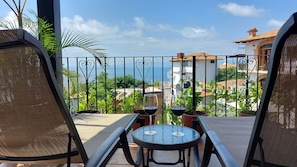 A balcony with a table and chairs, overlooking a residential area with houses and greenery.