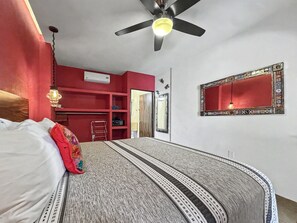Un dormitorio con cama, ventilador de techo, pared roja, espejo y puerta.