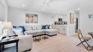 A modern living room with a sofa, coffee table, and chairs. There is a kitchen area with a microwave and a refrigerator. - ⭐1st Floor-Walk2Beach-Community Pool-1BR Shoeless Joe⭐ (Miramar Beach)
