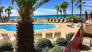 Un espace piscine avec des chaises longues et des palmiers, donnant sur une plage.