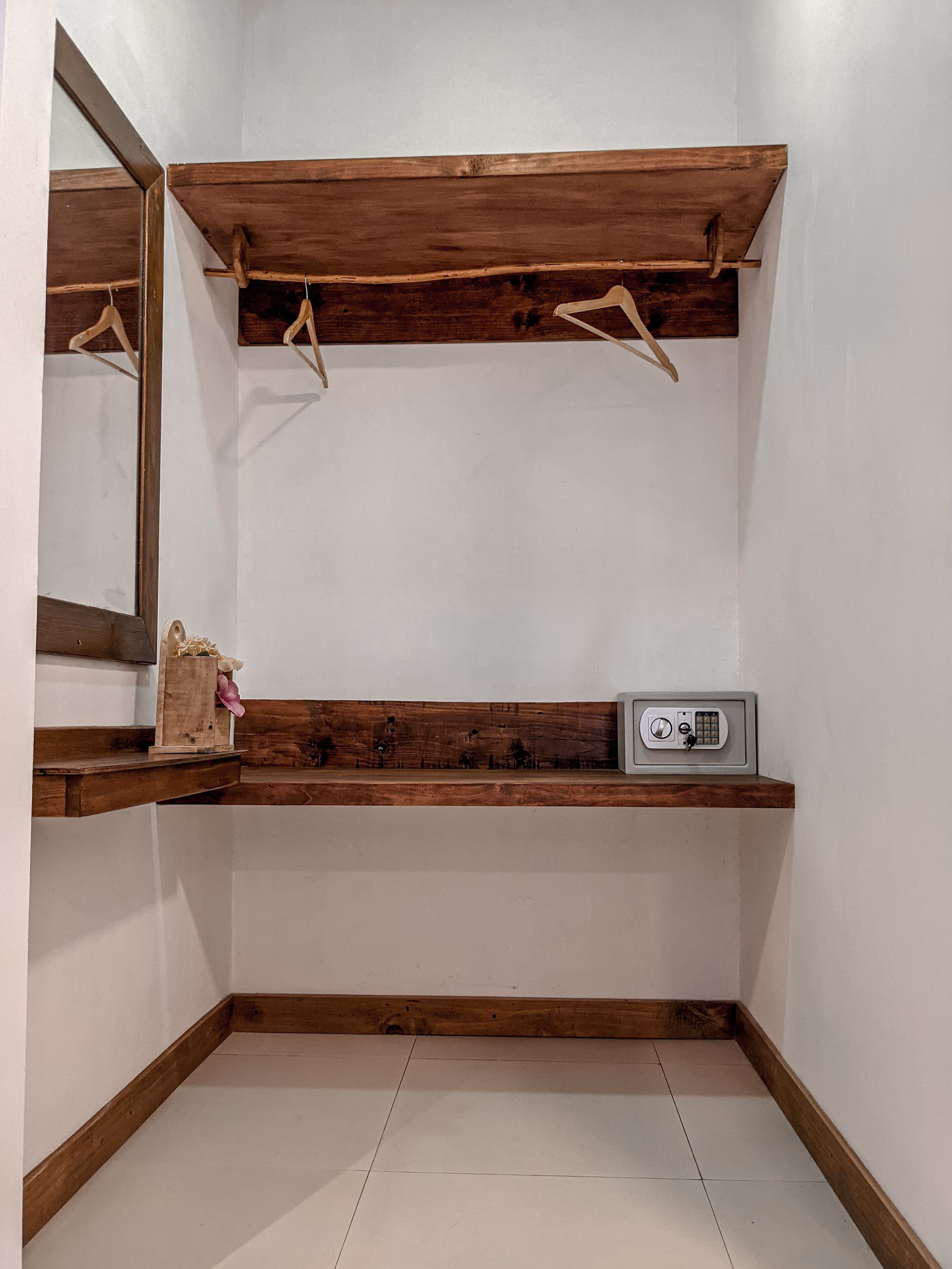 A corner room with a wooden shelf, a small safe, and a mirror.