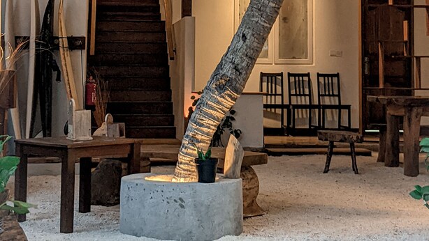 A rustic interior with a wooden staircase, a concrete planter with a palm tree, and a dining area with chairs and a table. - Dhoadhi Retreat (Thulusdhoo Island)