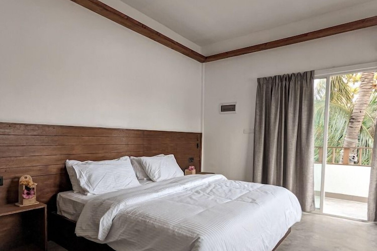Un dormitorio con cama, cabecera de madera, ventilador de techo y vista al exterior a través de una ventana.