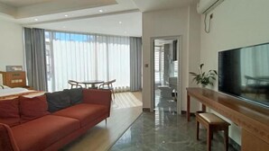 Una habitación de hotel moderna con un sofá rojo, un escritorio de madera, un televisor de pantalla plana y un ventanal con cortinas.