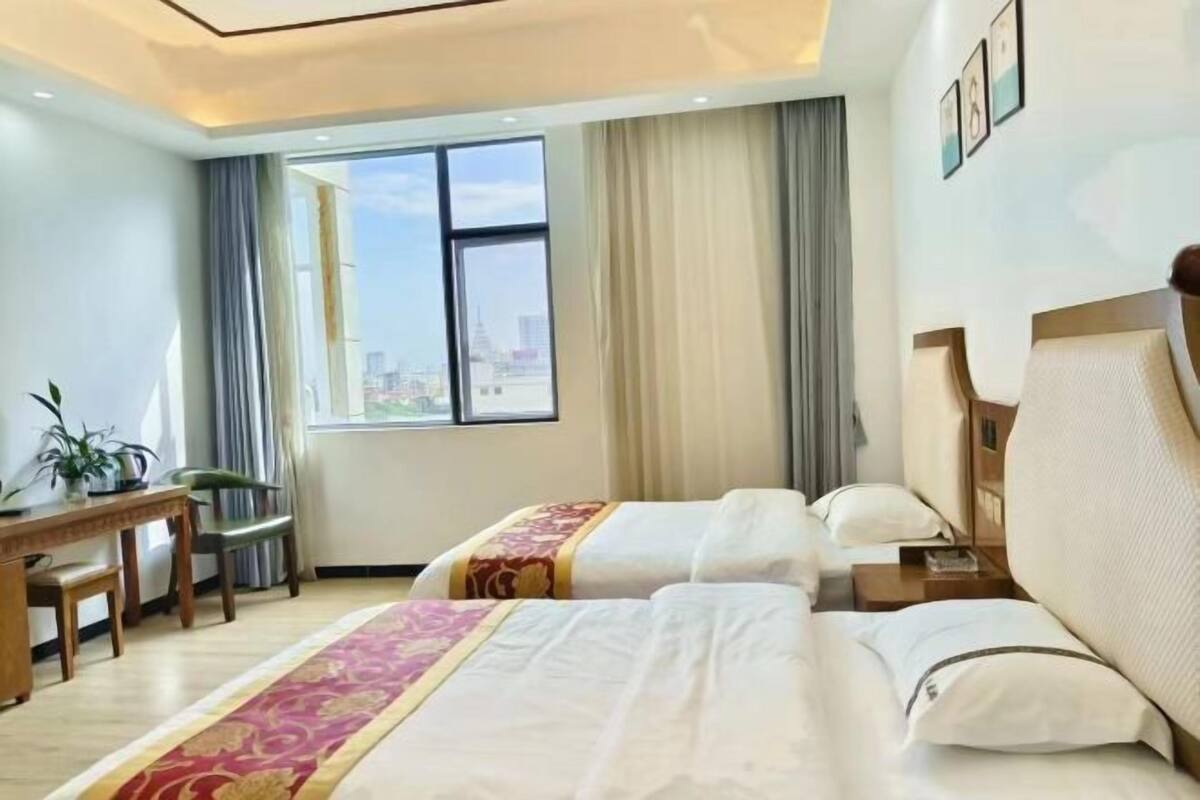 A hotel room with two beds, a desk, a chair, and a large window with a city view.