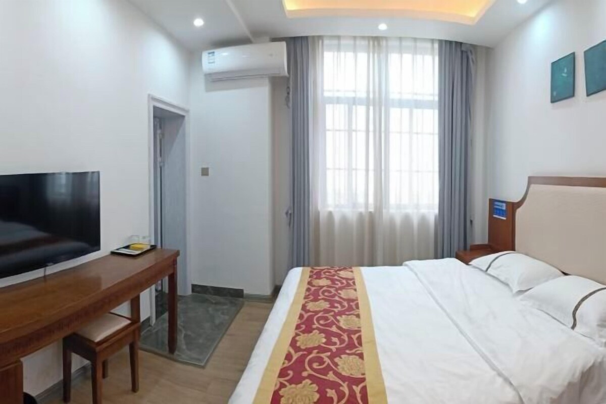 Quarto de hotel com cama, televisão, escrivaninha e janela com cortinas.