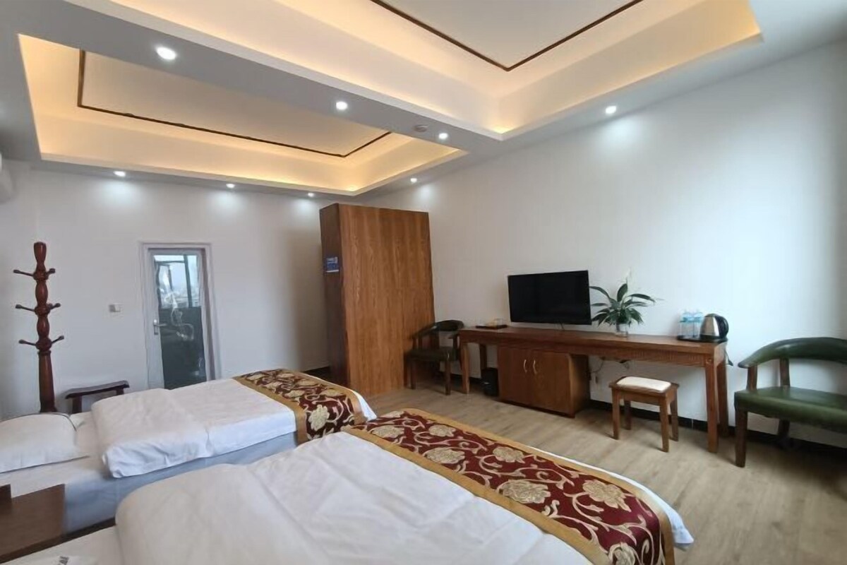 Quarto de hotel com duas camas, uma escrivaninha com televisão, uma cadeira e um guarda-roupa.