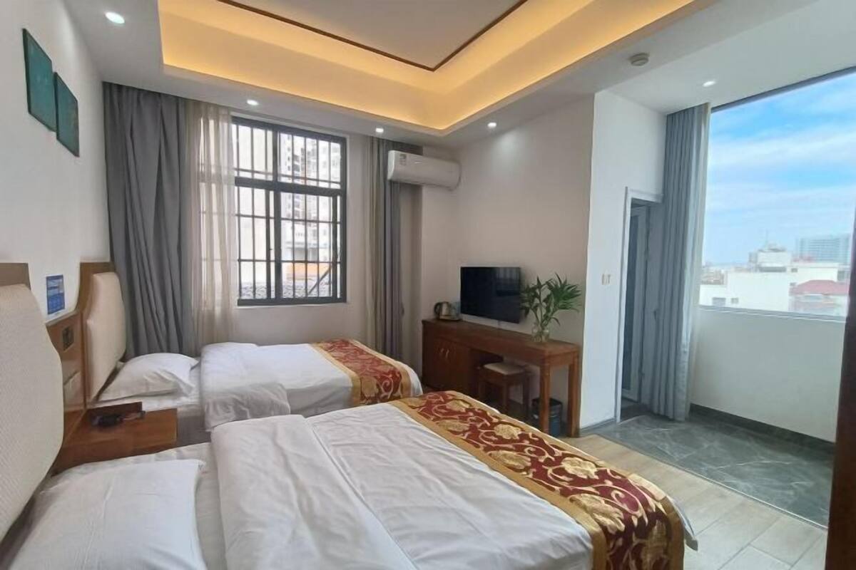 A hotel room with two beds, a desk with a TV, a window with curtains, and a balcony.